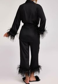 Czarny satynowy zestaw do wypoczynku z długimi rękawami i spodniami, z czarnymi piórowymi akcentami przy mankietach i u dołu. Regulowany pas z wiązaniem.
