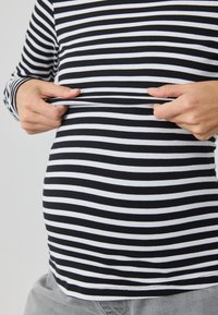 Black and white striped long-sleeve shirt, snug fit over a rounded belly, with hands adjusting the fabric. Soft, stretchy cotton material.