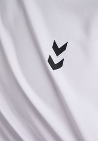 Vitt tyg med en slät textur som har en svart logotyp med två stiliserade chevroner. Designen är enkel och modern.