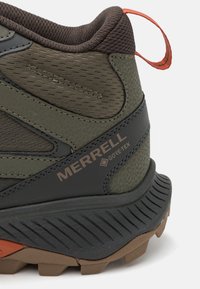 Buty trekkingowe Merrell z fakturowaną górą w kolorze szaro-brązowym, z logo Gore-Tex oraz gumową podeszwą z wyraźnym bieżnikiem. Akcenty w kolorze pomarańczowym.
