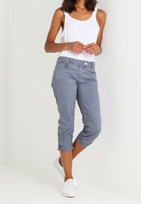 Lichtgrijze cropped broek met een gladde textuur, elastische manchetten, voorzakken en een knoopsluiting, gecombineerd met een wit tanktop en witte sneakers.