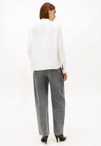 Blazer blanco de corte relajado, con mangas largas y abertura en la espalda. Combinado con vaqueros grises de cintura alta y zapatos de tacón negros.