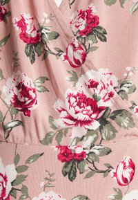 Tecido floral com grandes rosas vermelhas e brancas, acompanhadas de folhas verdes, sobre um fundo rosa suave; texturizado com um leve brilho.