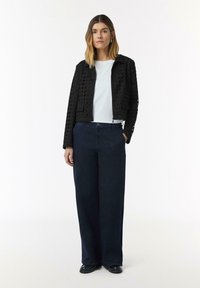 Zwarte cropped jas met een ruitpatroon, witte t-shirt en donkerblauwe wijde jeans, compleet met zwarte platform schoenen.
