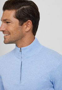 Jasnoniebieski rozpinany pulower z wysokim kołnierzem, wykonany z miękkiego, dzierganego materiału. Charakteryzuje się subtelną fakturą i starannym wykończeniem krawędzi.