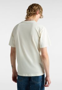 Kurzärmliges, hellcremefarbenes Baumwoll-T-Shirt mit Rundhalsausschnitt, glatter Textur und lockerer Passform, kombiniert mit gemusterten blauen Jeans.