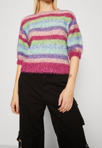 Meerlagige fuzzi gebreide trui met korte mouwen, voorzien van horizontale strepen in roze, groen, blauw en paars. Getextureerd, cropped ontwerp.