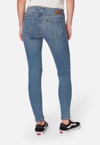 Vaqueros de mezclilla azul ajustados con cintura alta, con dos bolsillos traseros, textura desgastada y una etiqueta de cuero marrón en la cinturilla.