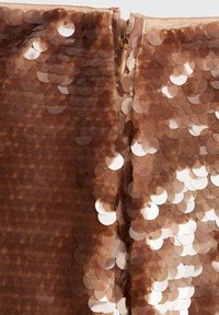 Tissu en sequins marron avec des sequins circulaires de différentes teintes, superposés pour ajouter de la texture, et doté d'une fermeture éclair au centre.