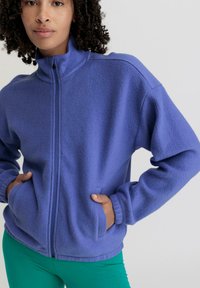 Fleece zip-up jack in levendig paars met hoge kraag, ribbelmanchetten en voorzakken. Zachte textuur en relaxte pasvorm voor comfort.
