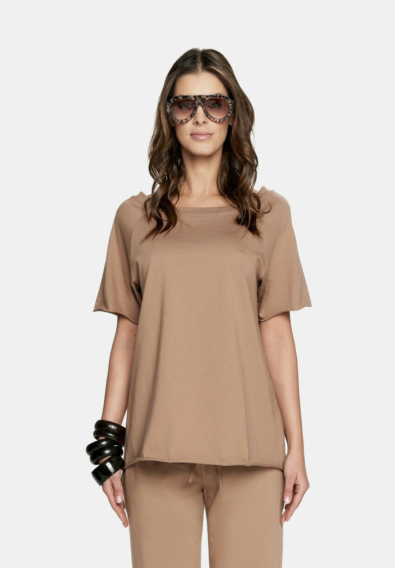 Brązowa koszulka z krótkim rękawem o luźnym kroju, z kwadratowym dekoltem i miękką teksturą. W połączeniu z dużymi, wzorzystymi okularami przeciwsłonecznymi.