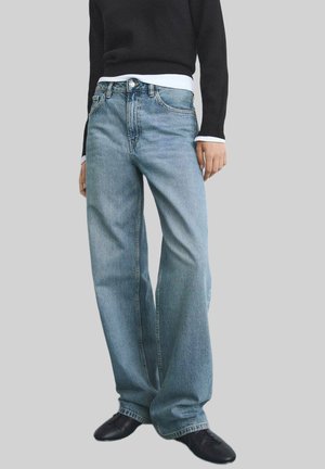 Vaqueros de denim azul claro con un corte holgado, que cuentan con un diseño de cinco bolsillos y detalles de costura sutiles. Combinados con un suéter negro y zapatos negros.