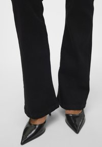 Zwarte flared broeken met een gladde textuur, gecombineerd met glanzende zwarte puntige hakken met een slanke stilettohak.