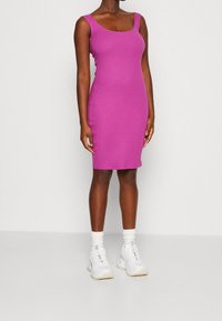 Robe rose ajustée à côtes avec des bretelles larges, longueur genoux, associée à des baskets blanches et des chaussettes de sport.