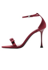 Sandal con tacco alto in raso rosso, con cinturino alla caviglia, tacco sottile, punta quadrata e un fiocco decorativo sulla fascia anteriore. Dettaglio della suola nera.