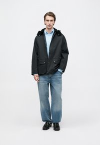 Dark gray jacket with a hood, two front pockets, and button fastening, worn over a light blue sweater and loose-fitting, light blue jeans.