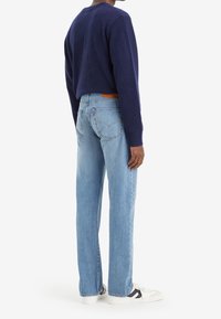 Suéter azul marino, vaqueros azul claro de corte relajado y zapatillas blancas con detalles en negro. Los vaqueros tienen un diseño clásico y un parche con logotipo en la parte trasera.