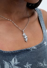 Hõbedane ripats kaelakee, millel on keeruline põimimisdisain koos graveeritud detailidega, rippumas ovaalsest linkide ahelast.