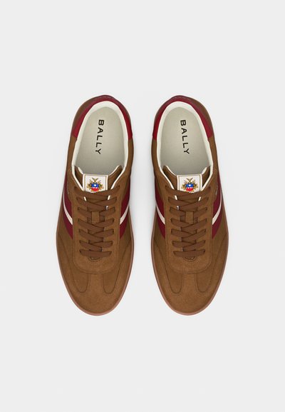 Ζευγάρι καφέ σουέντ αθλητικά παπούτσια με κόκκινες και λευκές ρίγες, καφέ κορδόνια που ταιριάζουν και επωνύμες εσωτερικές σόλες με την ένδειξη "BALLY".