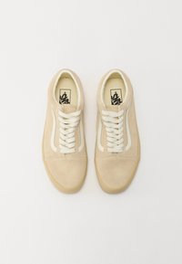 Beige mokkasiinikenkä, jossa on valkoiset nauhat ja sivupainatus. Pyöreä varvasosa, litteä kumipohja ja teksturoitu päällinen. Sisäosassa on brändilogo.