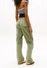 Vihreät cargo-housut, joissa on rento leikkaus, useita taskuja ja nyöri helmaassa. Yhdistetty raidalliseen, olkaimettomaan toppiin.