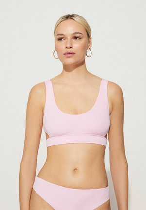 Hellrosa gerippter Bralette mit breiten Trägern, weitem Ausschnitt und ausgeschnittenen Seiten. Kombiniert mit passenden Bikinislips. Sanfte Textur.
