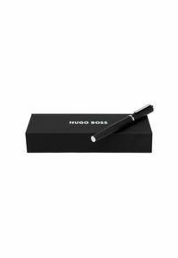 Bolígrafo negro con empuñadura texturizada colocado sobre una caja negra. La caja presenta la marca "Hugo Boss" en blanco, con un clip plateado brillante en el bolígrafo.
