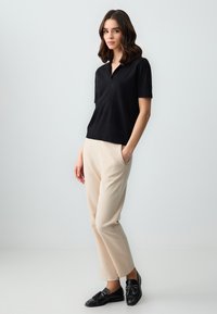 Polo shirt nero a maniche corte, design aderente; abbinato a pantaloni beige a gamba affusolata e mocassini neri. Tessuto liscio e dettagli sobri.
