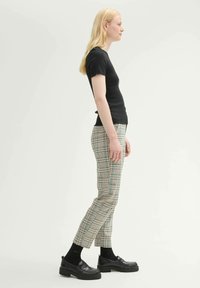 Black ribbed short-sleeve top, plaid trousers in beige with green and blue accents, black shoes, and ankle-length black socks.