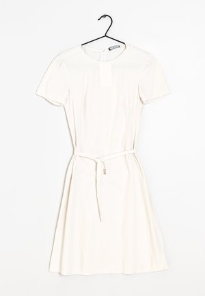 Robe blanche à manches courtes avec col rond et ceinture fine, suspendue sur un cintre noir contre un fond blanc.