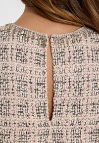 Geweven blouse in roze en crèmewit met gestructureerde stof en open rug. Heeft een decoratieve kraalaccent rond de halslijn.