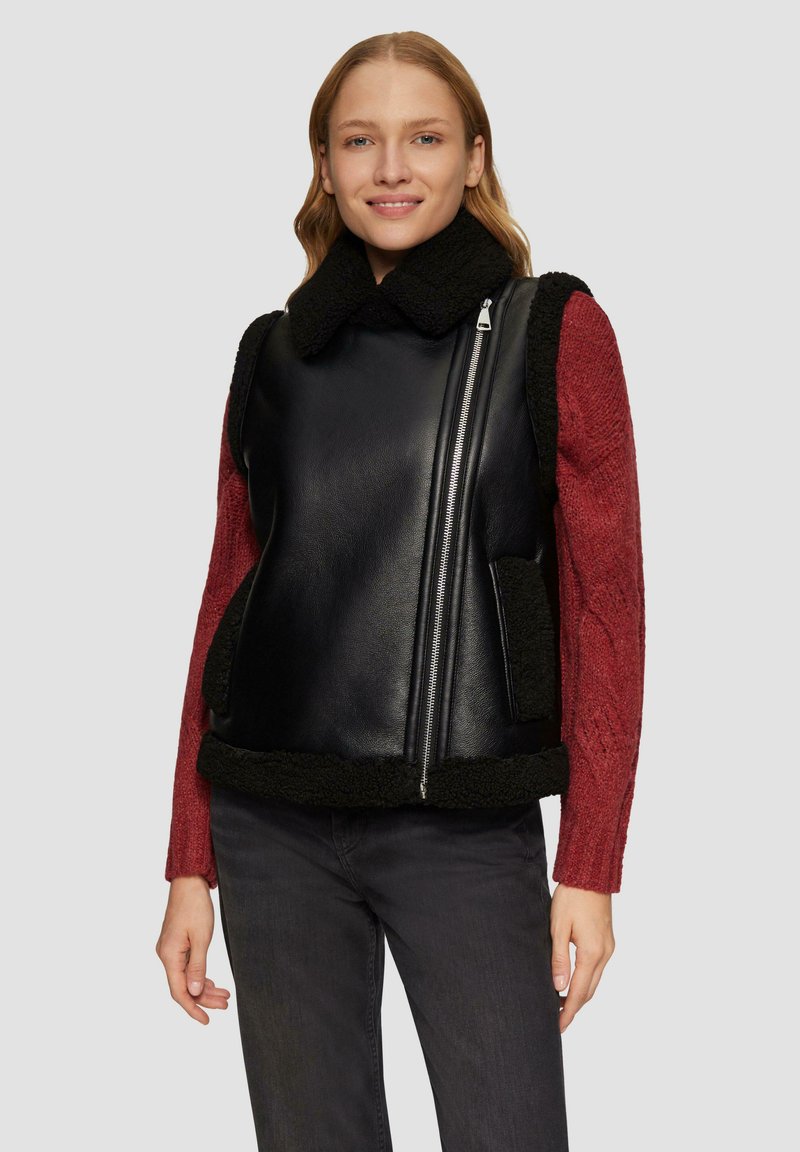 Zwarte leren gilet met schapenvachtaccenten, hoge kraag en zijzakken. Draag het over een gestructureerde rode trui en combineer het met donkere jeans.