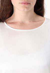 Top bianco a maniche corte con una texture liscia e leggermente trasparente, dotato di scollatura rotonda e un sottile bordino a contrasto.