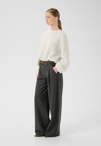 Lagani, kremasti pulover s opuštenim krojem. Hlače visoki struk tamnosive boje s vertikalnim prugama, učvršćene smešnim remenom.