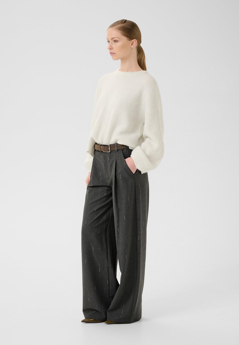 Leichter, cremefarbener Pullover mit lockerer Passform. Hoch taillierte, dunkelgraue Hose mit vertikalen Streifen, gesichert mit einem braunen Gürtel.