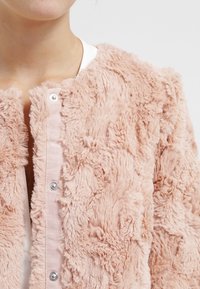 Kurtka z futra syntetycznego w jasnoróżowym kolorze, z teksturowaną powierzchnią, z przodu zapinaną na napy oraz okrągłym dekoltem.