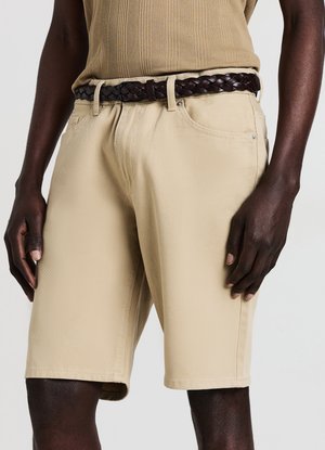 Beige Baumwollshorts mit geradem Schnitt und subtiler Textur, ausgestattet mit Seitentaschen und einem dunklen geflochtenen Ledergürtel in der Taille.