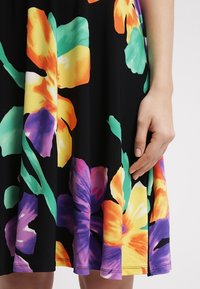 Kwiatowa sukienka z dzianiny na czarnym tle. Posiada żywe pomarańczowe, fioletowe i zielone kwiaty. Gładki materiał i swobodny fason.