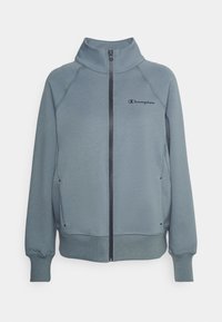 Ljusblå zip-up sweatshirt med hög krage, tillverkad av mjukt tyg, med en svart logotyp på bröstet och ribbade ärmslut och fåll.