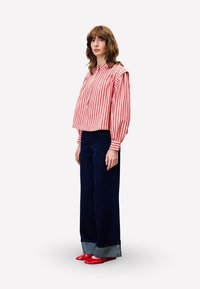 Rood-wit gestreepte cropped blouse met ballonmouwen, gecombineerd met donkerblauwe wide-leg jeans met omgeslagen onderkant en rode schoenen.