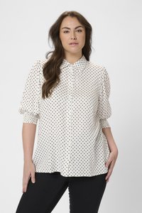 Chemise blanche à boutons avec des pois noirs, présentant des manches bouffantes et un col classique. Tissu doux, coupe décontractée et ourlet arrondi.