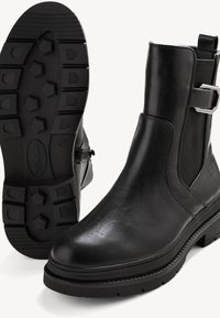 Bottines en cuir noir avec semelles en caoutchouc épaisses, panneaux élastiques latéraux et boucle argentée, vues de côté et de la semelle.