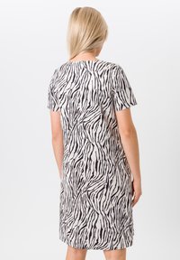 Kurzärmeliges Kleid mit Zebra-Muster, das schwarze und weiße Streifen zeigt. Die lockere Form fällt knapp über das Knie. Weicher Stoff.