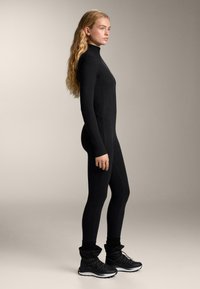 Body negru, mulat, cu mâneci lungi și guler înalt. Purtat cu bocanci negri, groși, cu șireturi, prevăzuți cu manșetă moale. Textură netedă.