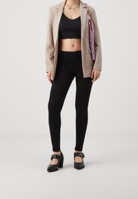 Blazer beige, top corto negro, jeans skinnies de tiro alto negros y zapatos de tacón negros con correas en el tobillo. Bolso texturizado morado.
