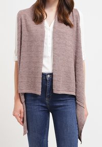 Leichter, offen gestrickter Schal in gedämpftem Mauve, mit einem strukturierten Muster und asymmetrischem Saum. Getragen über einer weißen Bluse und blauen Jeans.