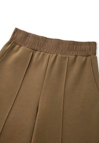 Pantalones jogger marrones con una amplia cinturilla elástica, textura suave, pliegues frontales y bolsillos laterales. Diseño casual adecuado para un uso relajado.