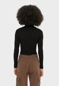 Maglione a collo alto nero a coste con maniche lunghe, abbinato a pantaloni cargo marroni con tasche a toppa e una vestibilità relax.