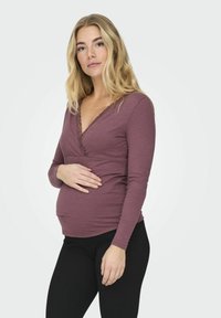 Rózsaszín, bordázott, hosszú ujjú kismama póló V-nyakkivágással és csipkés díszítéssel. Fekete, szoros leggings-szel párosítva. Puha tapintású.