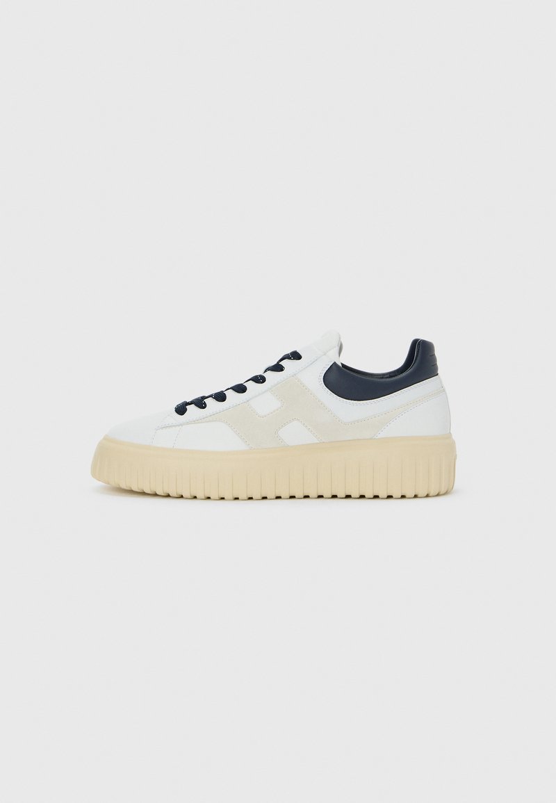 Sneaker bianche basse con dettaglio laterale in suede beige, lacci neri, colletto del tallone nero e suola in gomma beige spessa.